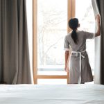Female housekeeping opening window curtains in the hotel room